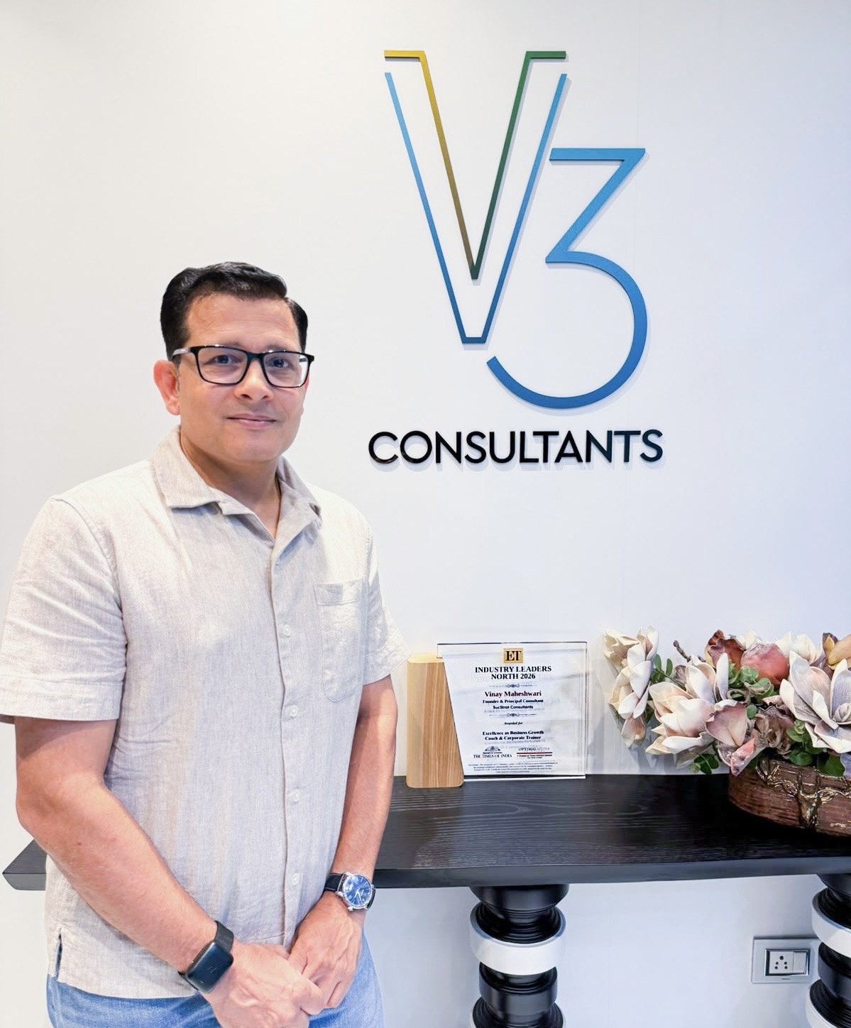 Vinay Maheshwari standing beside the V3 Consultants sign at his office, next to his ET Industry Leaders North 2026 award